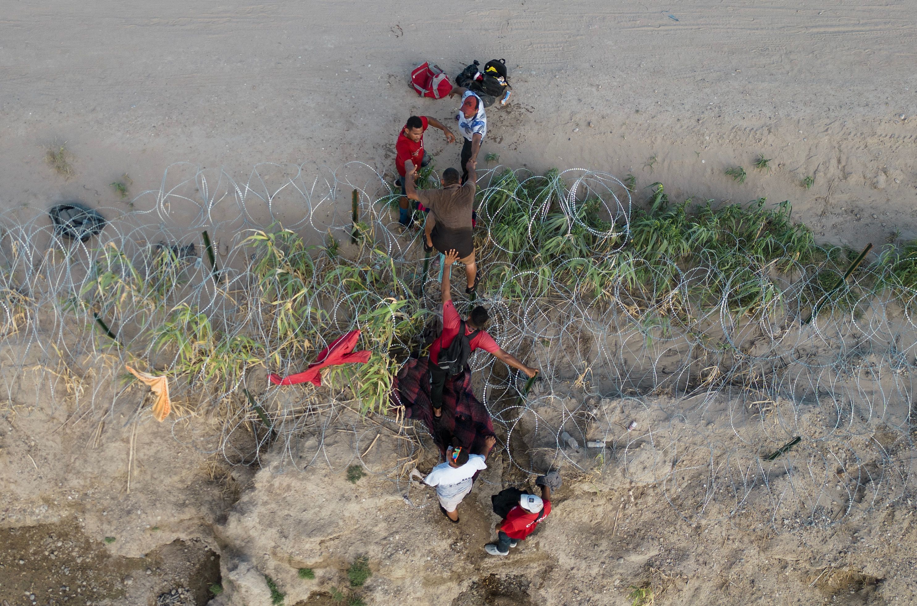 Aerial view of migrants crossing a border fence.